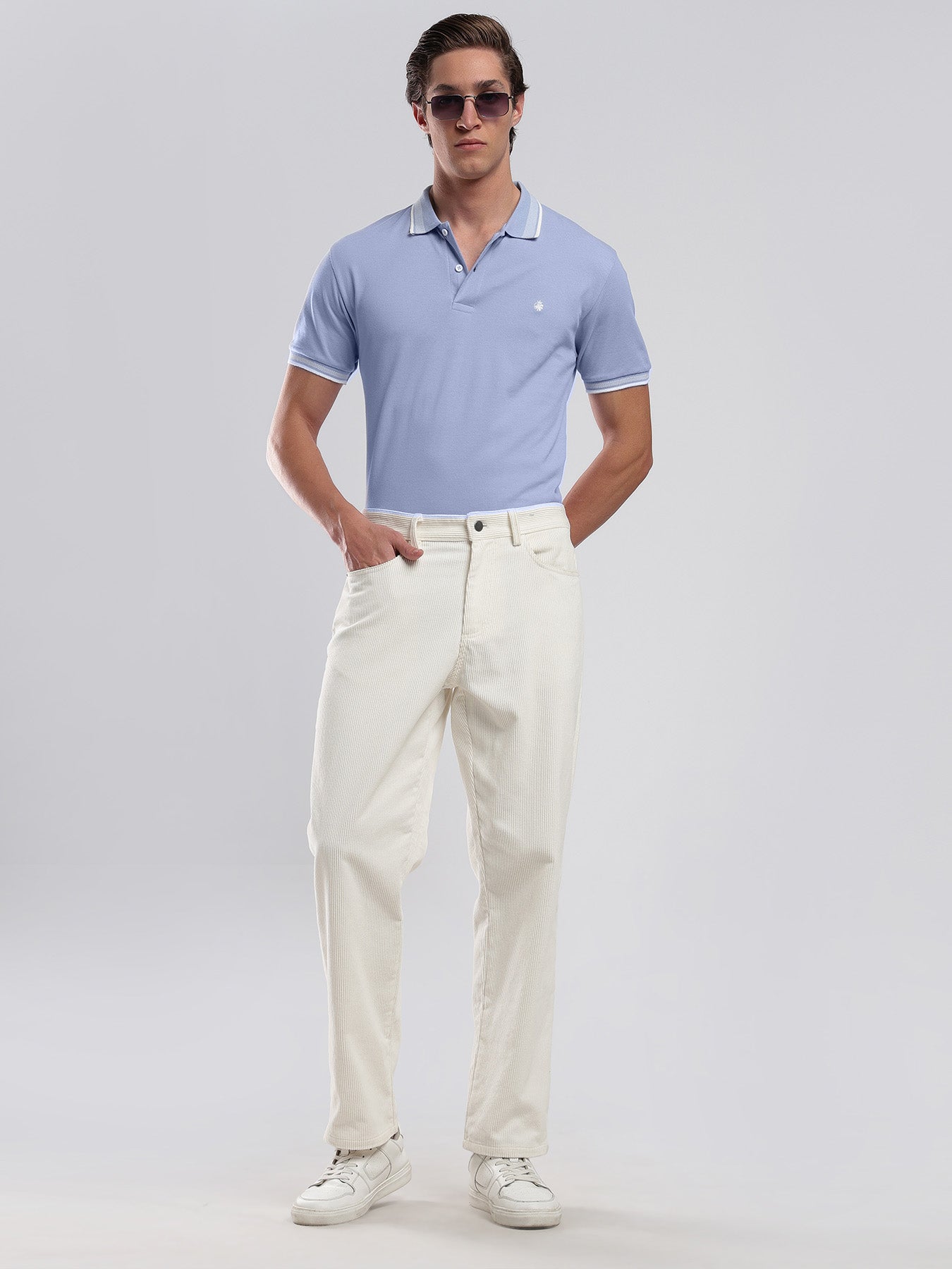 Man wearing a light blue polo shirt and white pants on a gray background