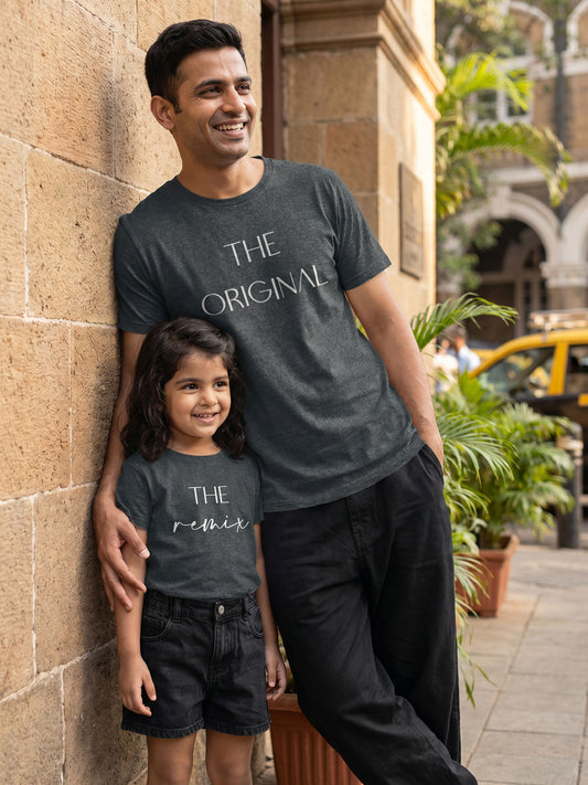 Man and child wearing matching dark gray t-shirts with text, standing against a stone wall.