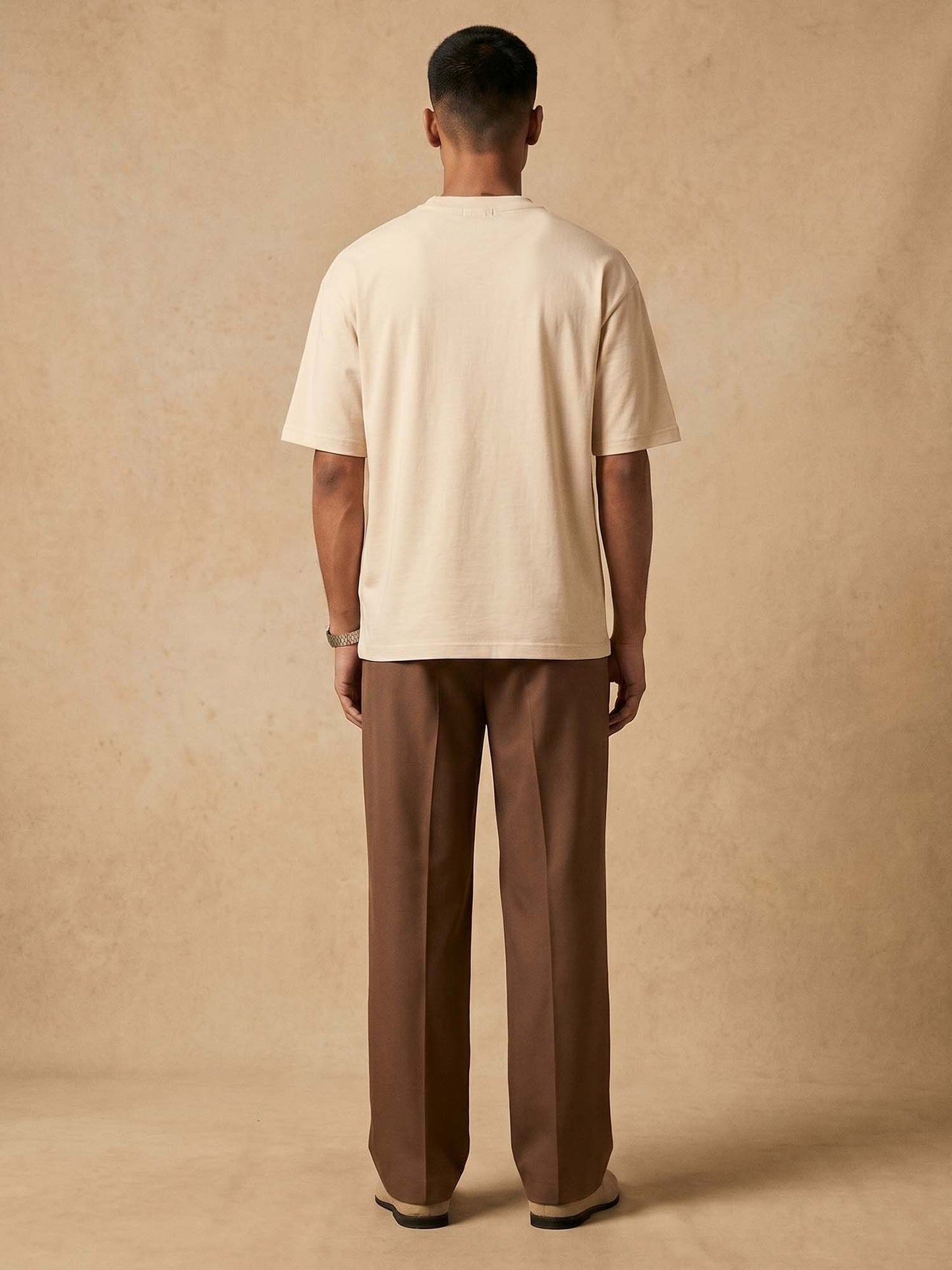 Man wearing a beige t-shirt and brown pants against a beige background