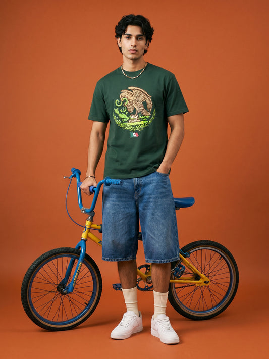 Man wearing a green t-shirt with a graphic design, standing next to a bicycle on an orange background