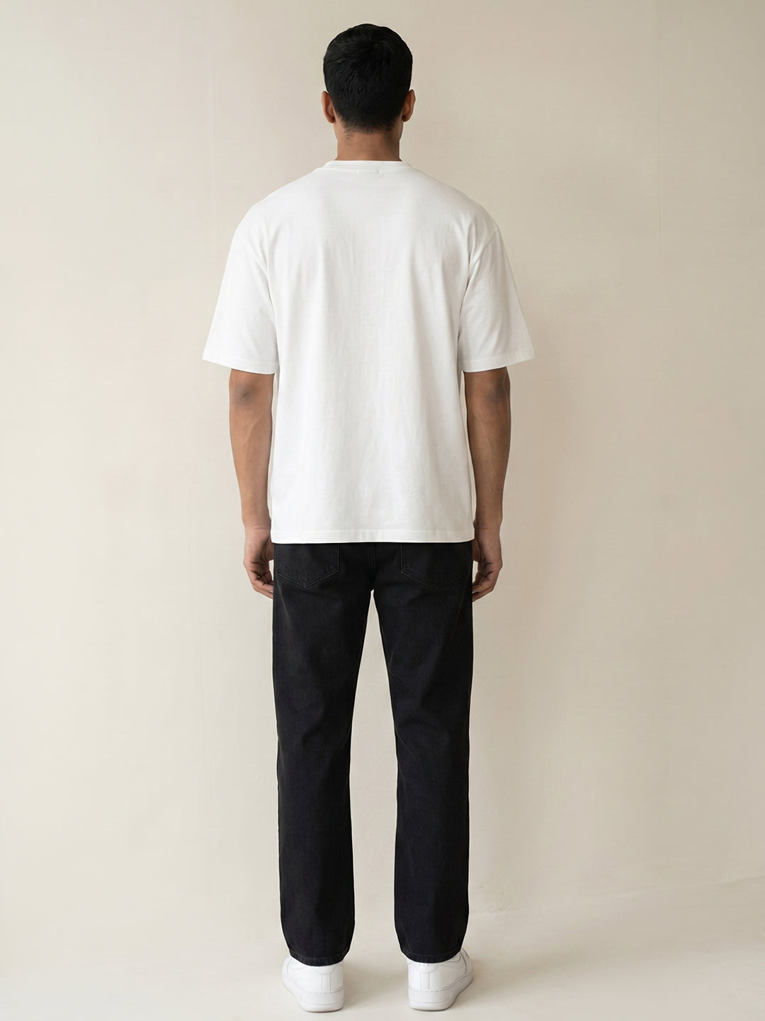 Person wearing a white t-shirt and black pants on a beige background