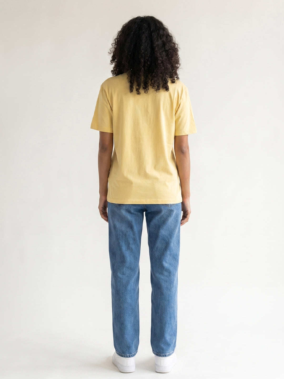 Person wearing a yellow t-shirt and blue jeans from behind on a white background