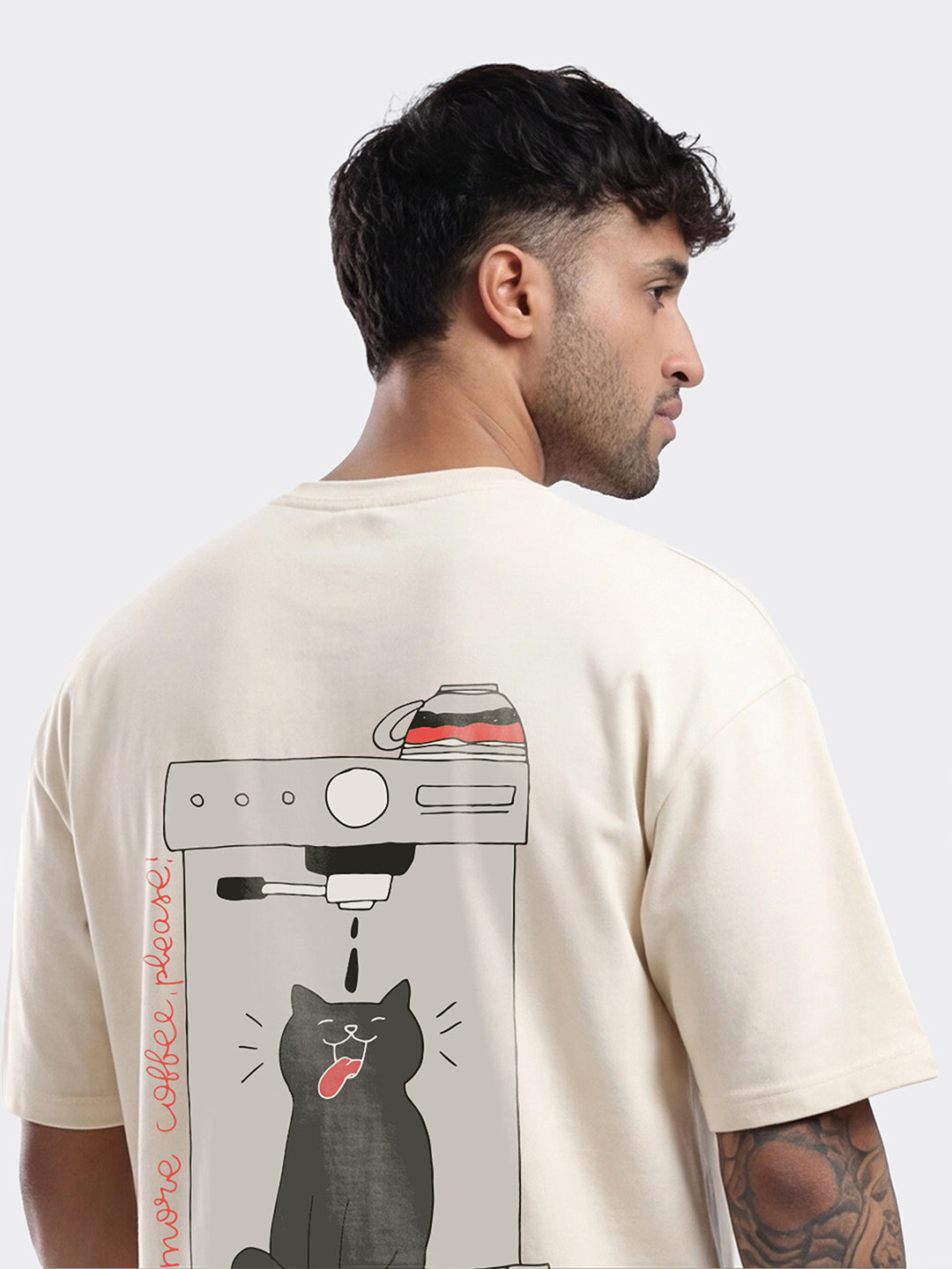 Man wearing a beige t-shirt with a graphic design on the back, featuring a coffee machine and a cat.