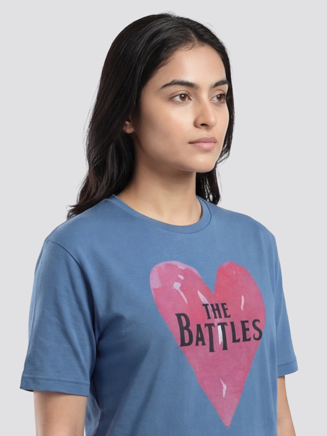 Person wearing a blue t-shirt with a pink heart and 'The Battles' text on a plain background