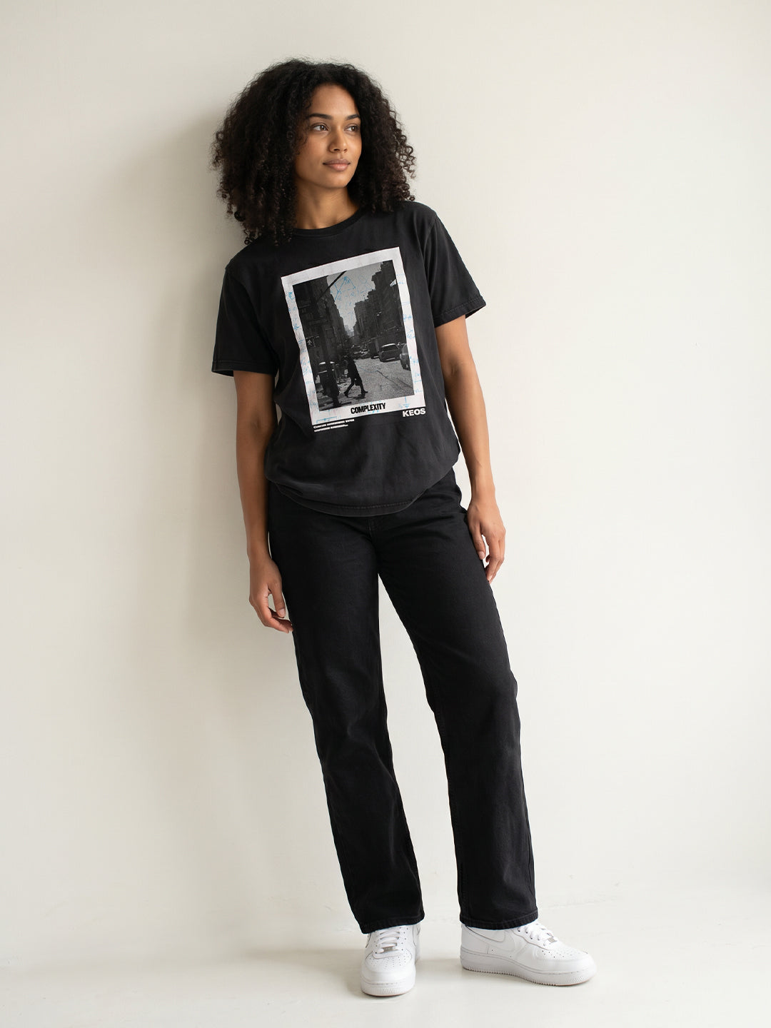 Person wearing a black t-shirt with a graphic design, black pants, and white sneakers on a plain background