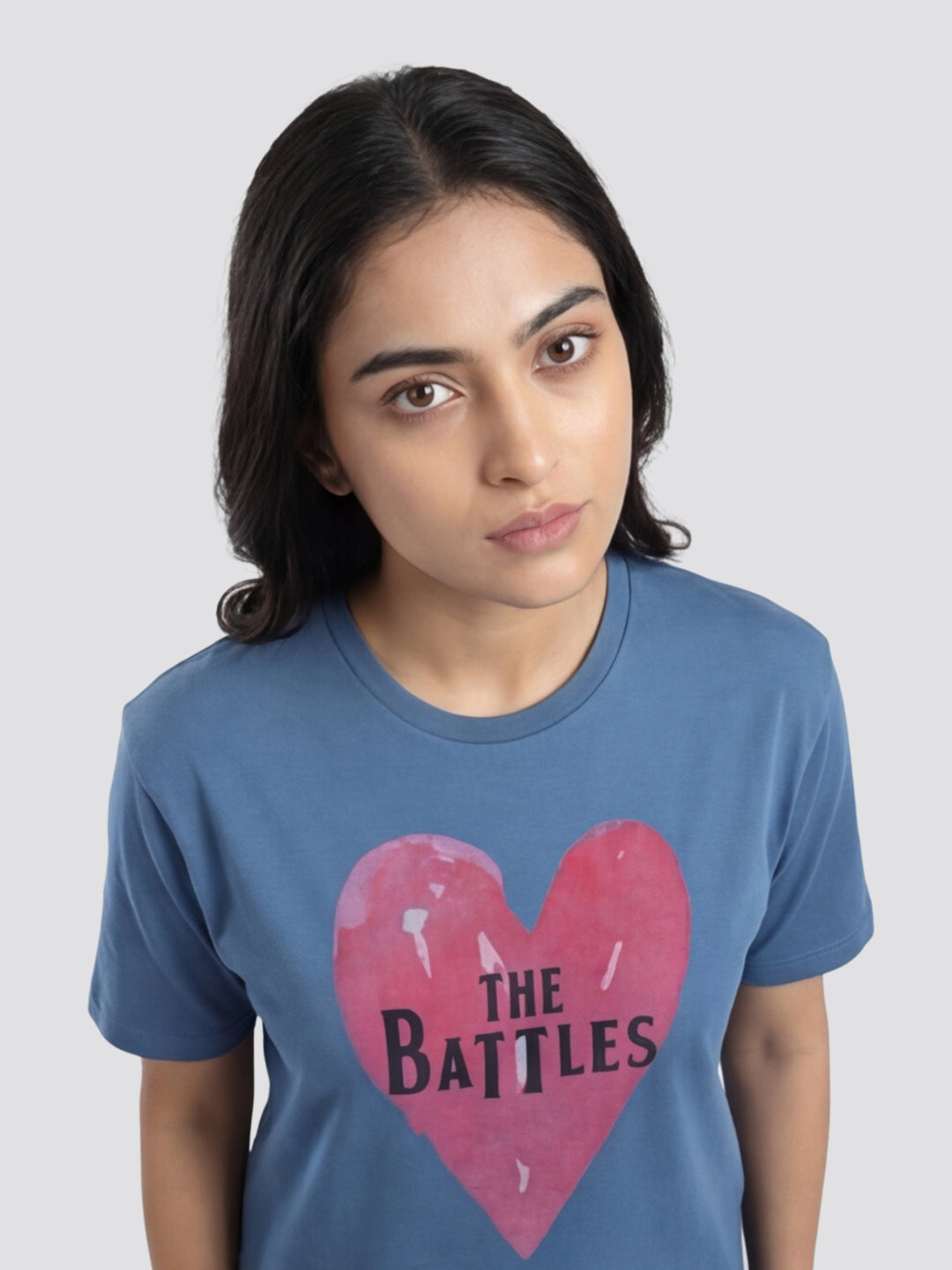 Person wearing a blue t-shirt with a pink heart and 'The Battles' text on a plain background