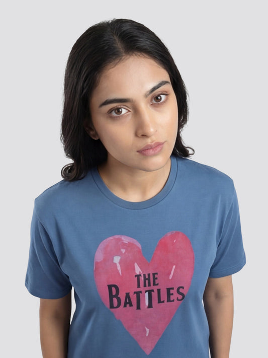 Person wearing a blue t-shirt with a pink heart and 'The Battles' text on a plain background