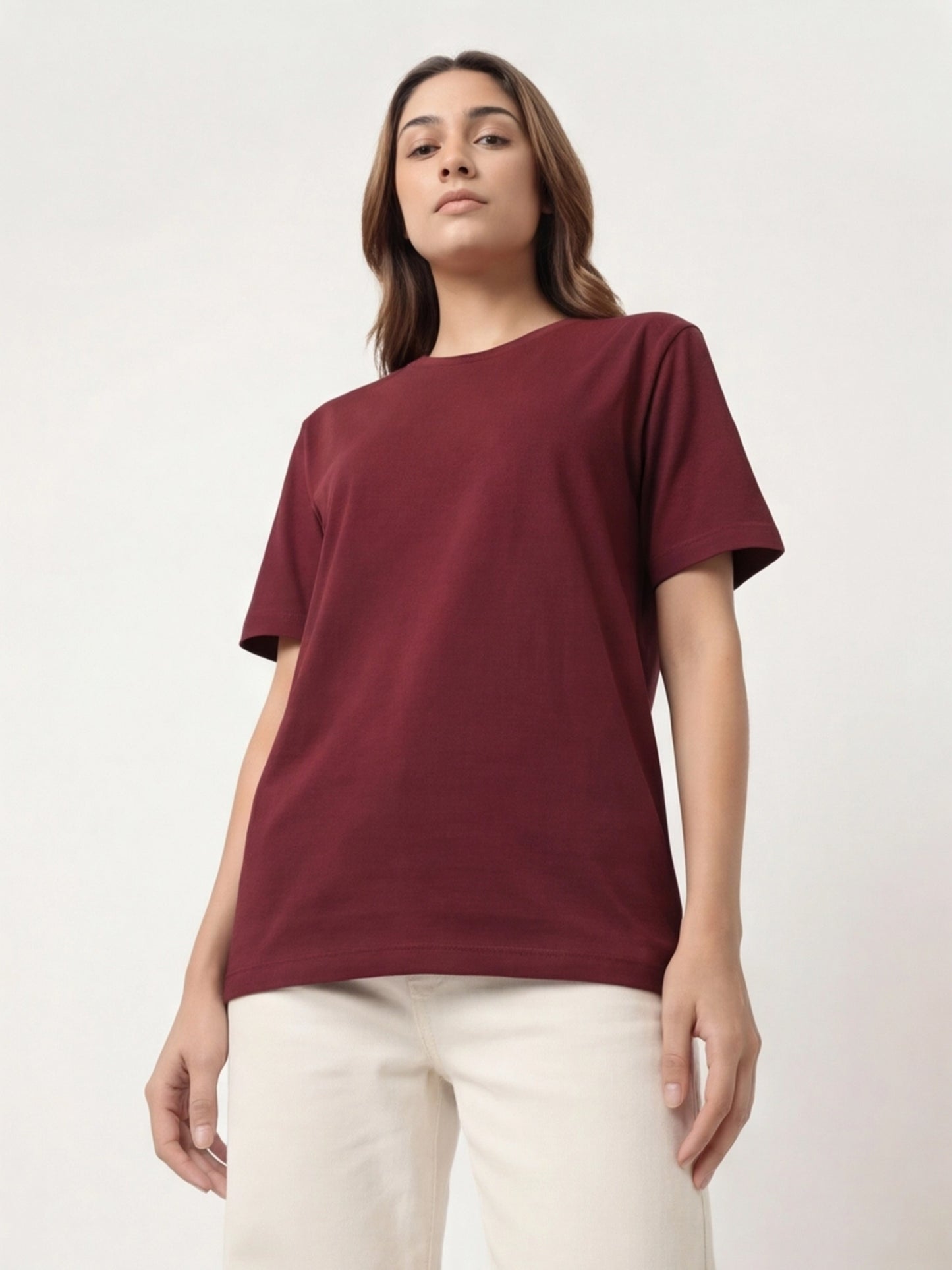 Woman wearing a maroon t-shirt and white pants on a light gray background