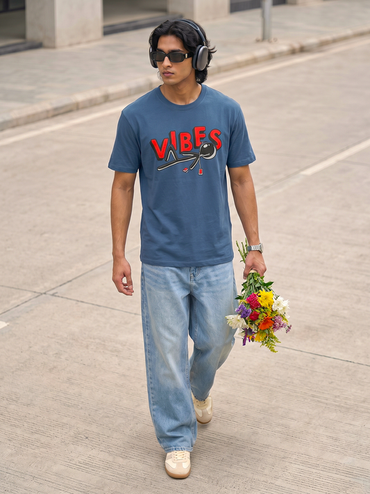 Blue Vibes Graphic T-Shirt Keos blue graphic t-shirt paired with relaxed light wash denim and white sneakers. A modern streetwear look featuring headphones, fresh flowers and effortless city style, blending music culture, casual fashion and youthful self-expression.
