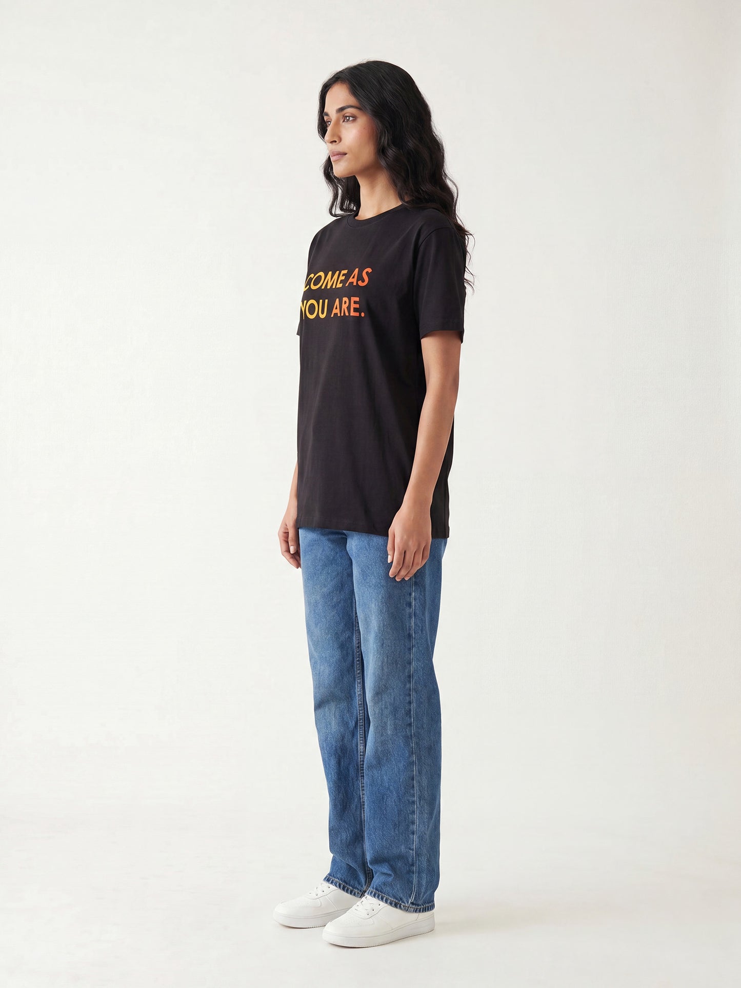 Side profile of women’s black Keos Come As You Are graphic tee with yellow orange chest text, styled with relaxed blue denim.