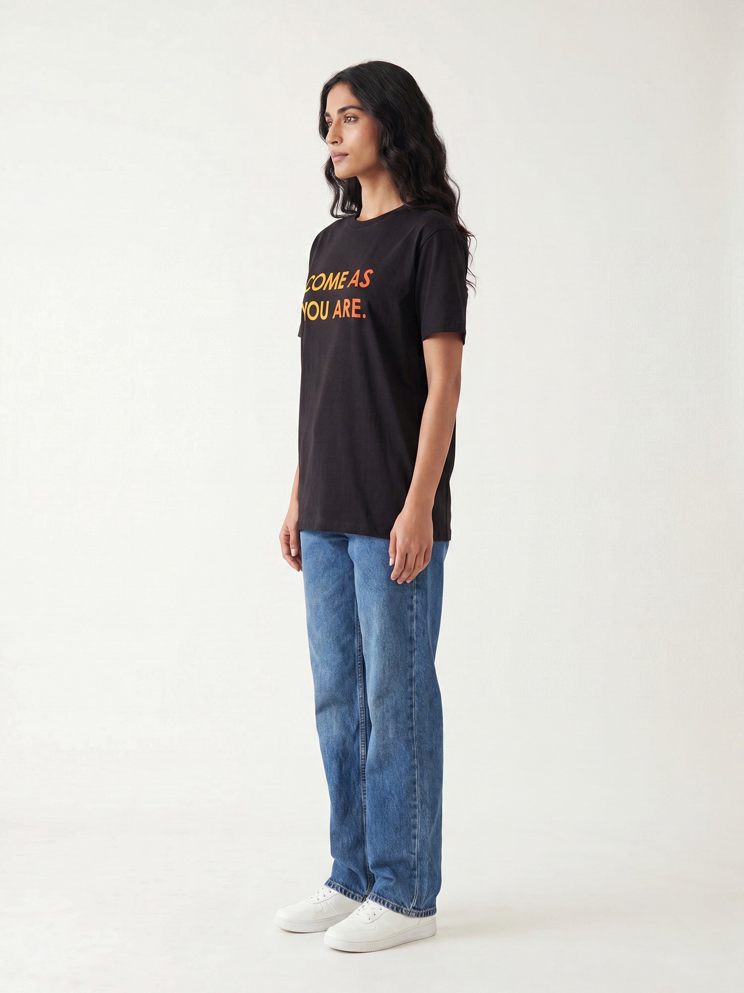 Side profile of women’s black Keos Come As You Are graphic tee with yellow orange chest text, styled with relaxed blue denim.
