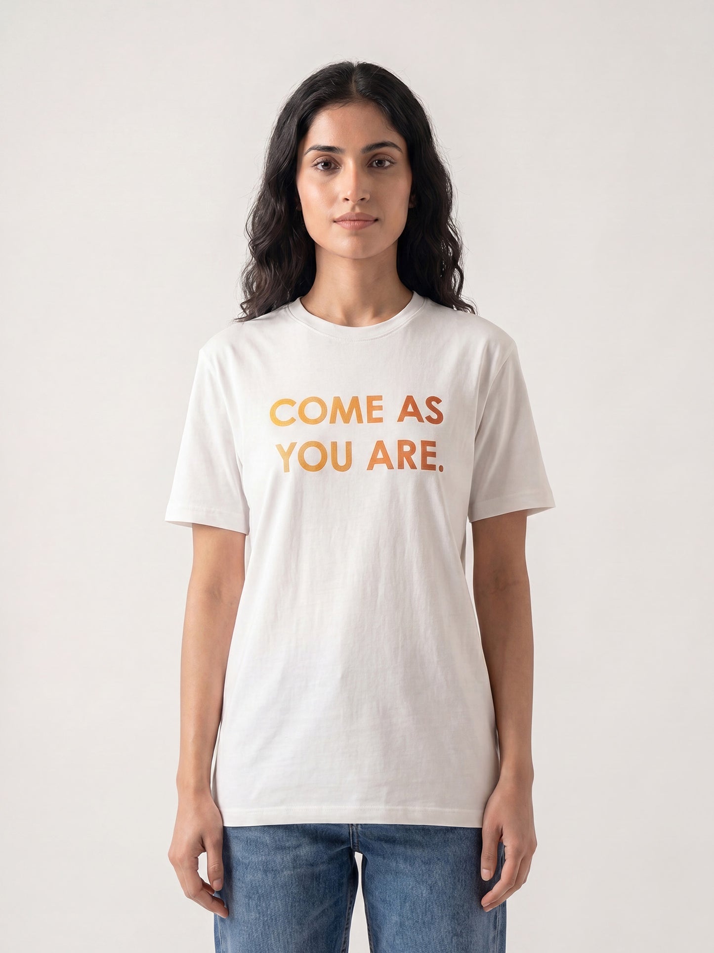 Indian female model wearing Keos Come As You Are white graphic t-shirt with yellow orange text print, styled with blue denim jeans.