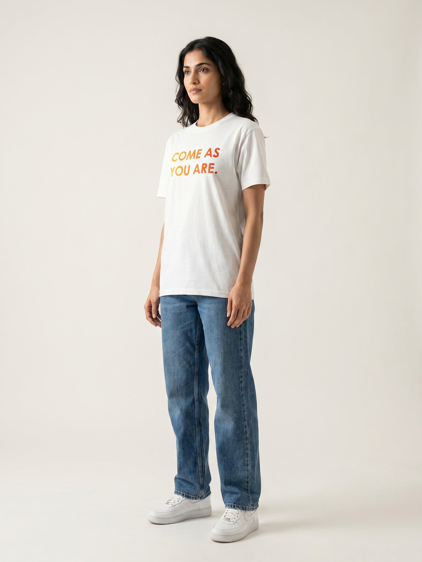 Side profile of women’s white Keos Come As You Are graphic tee with yellow orange chest text, styled with relaxed blue denim.