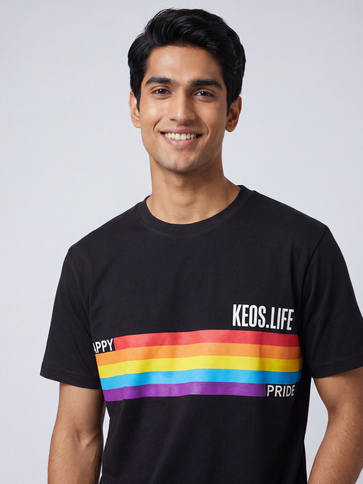 Close-up of Keos Happy Pride black cotton t-shirt showing rainbow stripe graphic, KEOS.LIFE branding, crew neck, and soft fabric texture.