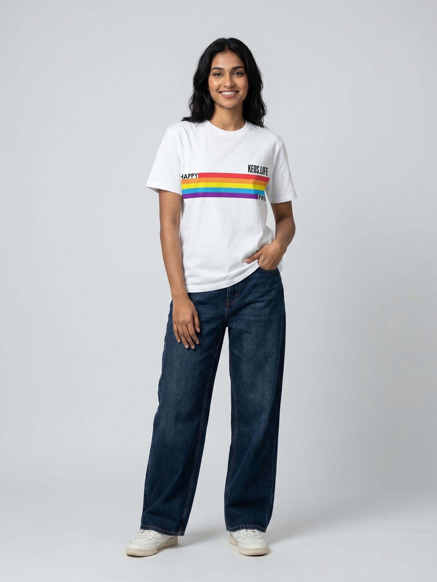 Keos Happy Pride white cotton graphic t-shirt featuring rainbow Pride stripe artwork, styled with wide-leg blue denim and white sneakers.