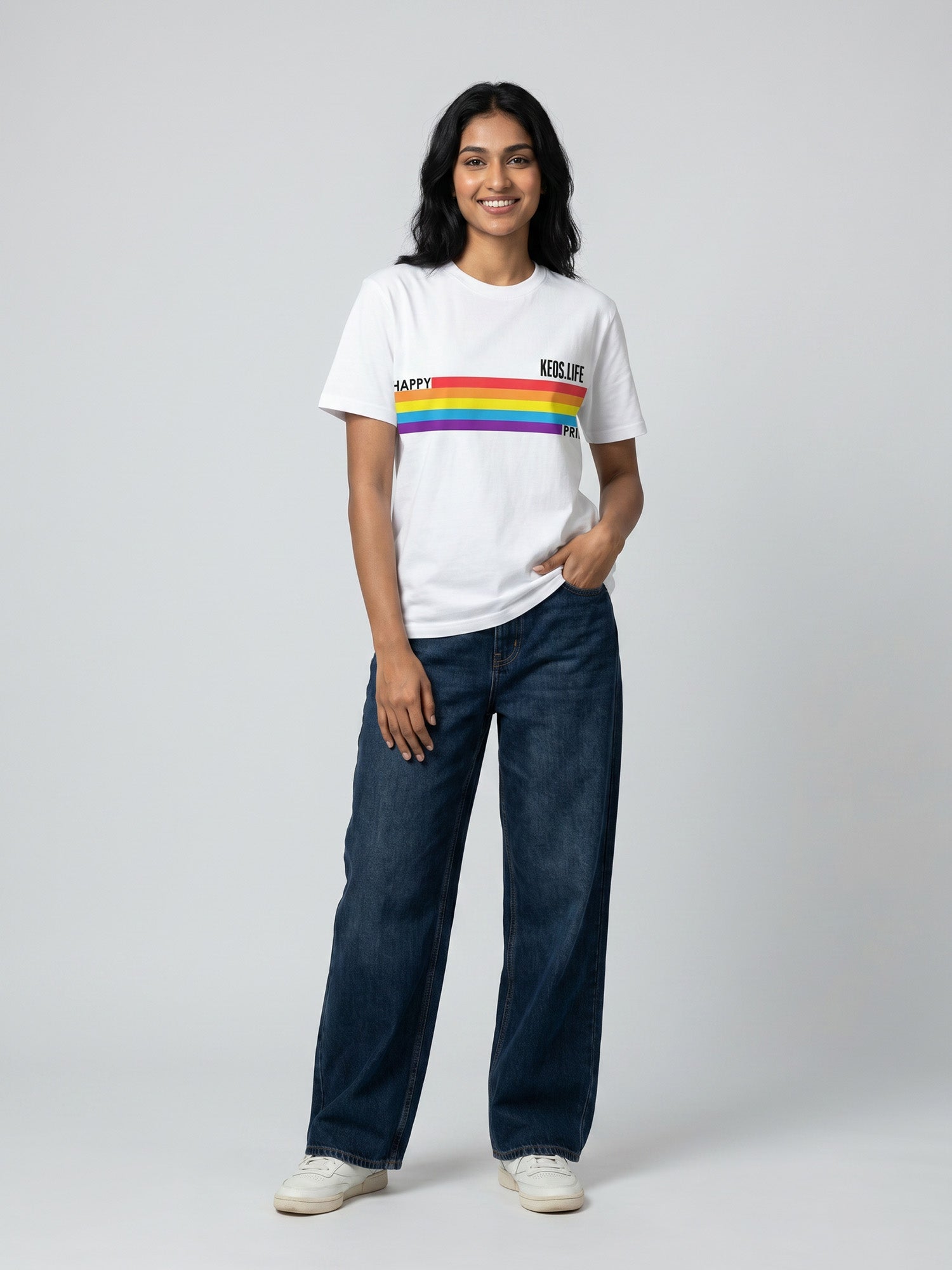 Keos Happy Pride white cotton graphic t-shirt featuring rainbow Pride stripe artwork, styled with wide-leg blue denim and white sneakers.
