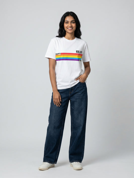 Keos Happy Pride white cotton graphic t-shirt featuring rainbow Pride stripe artwork, styled with wide-leg blue denim and white sneakers.