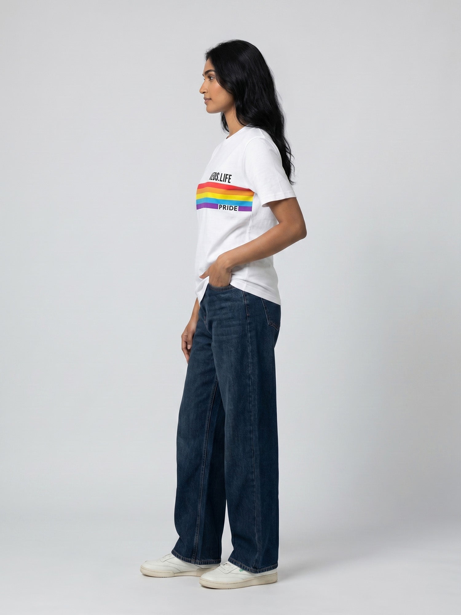 Side profile of women’s white Keos Happy Pride graphic tee with colourful rainbow chest print, styled with relaxed blue jeans.