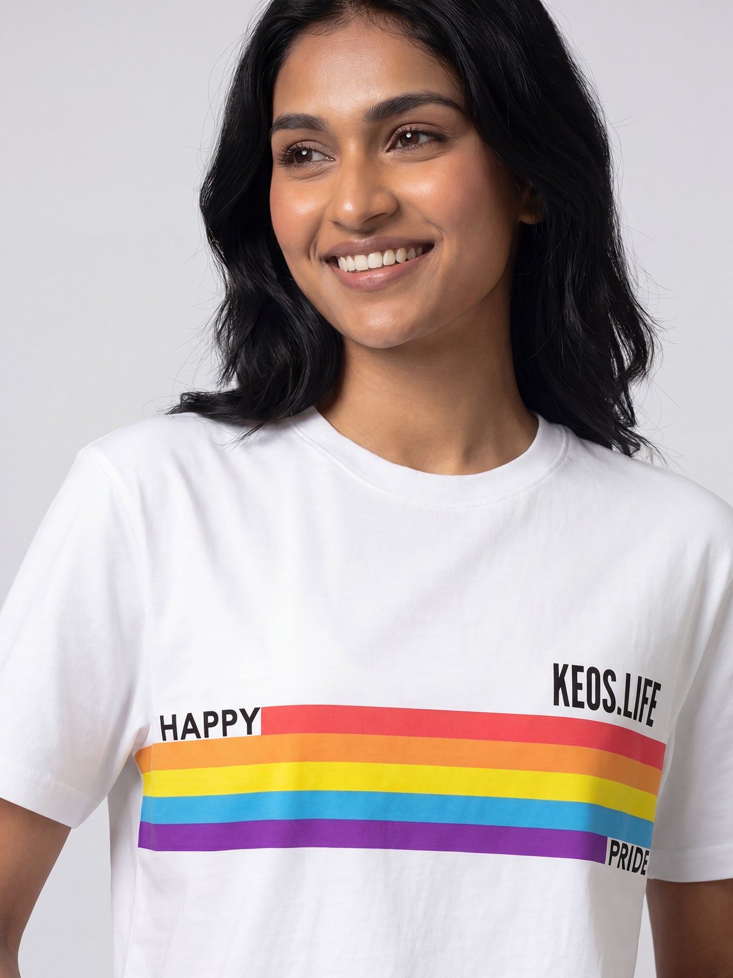 Close-up of Keos Happy Pride white cotton t-shirt showing rainbow stripe graphic, KEOS.LIFE branding, crew neck, and soft fabric texture.