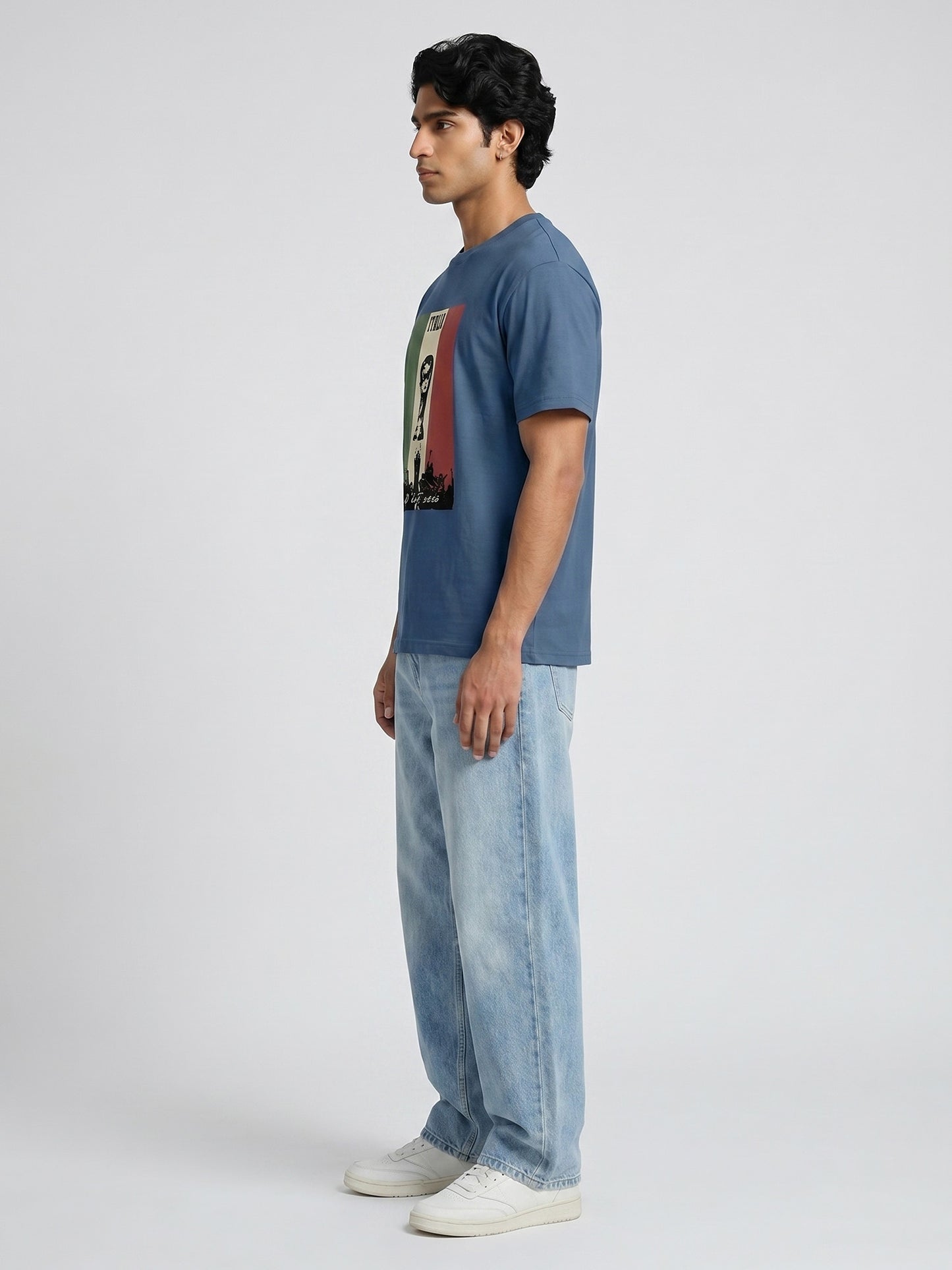 Man wearing a blue t-shirt with a graphic design and light blue jeans on a white background