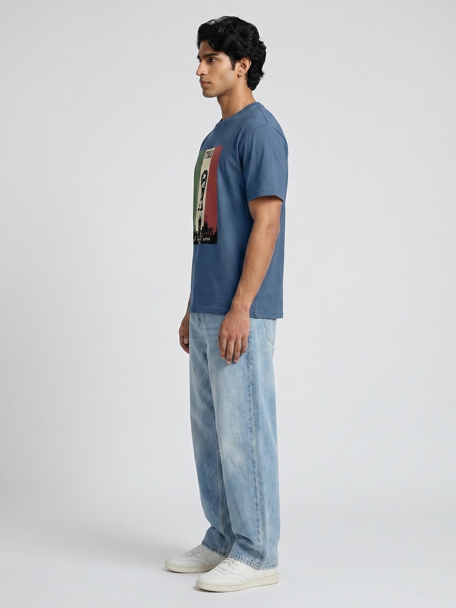 Man wearing a blue t-shirt with a graphic design and light blue jeans on a white background