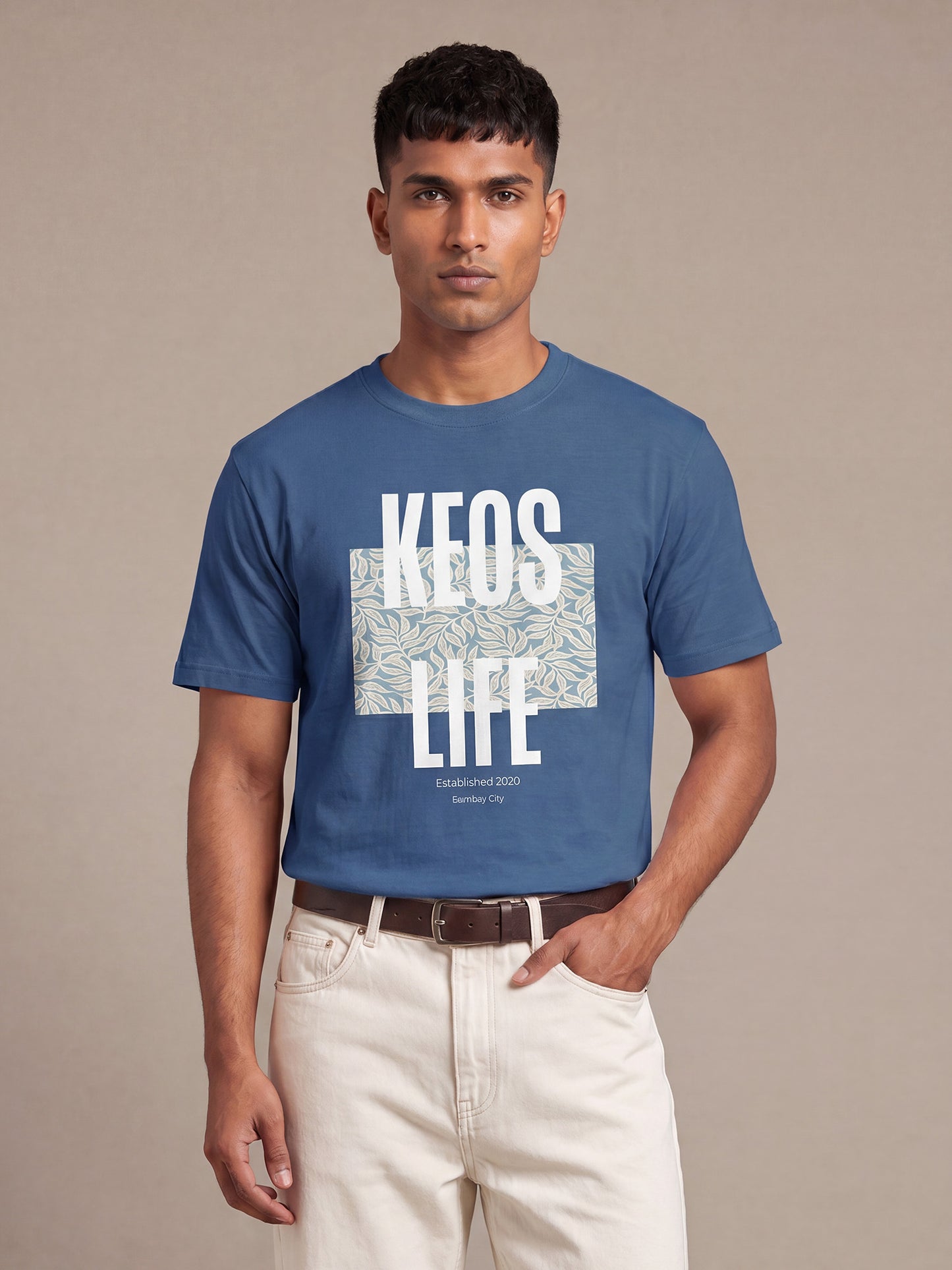 Indian male model wearing Keos Floral Block blue graphic t-shirt with white KEOS LIFE print and floral artwork, styled with off-white trousers.
