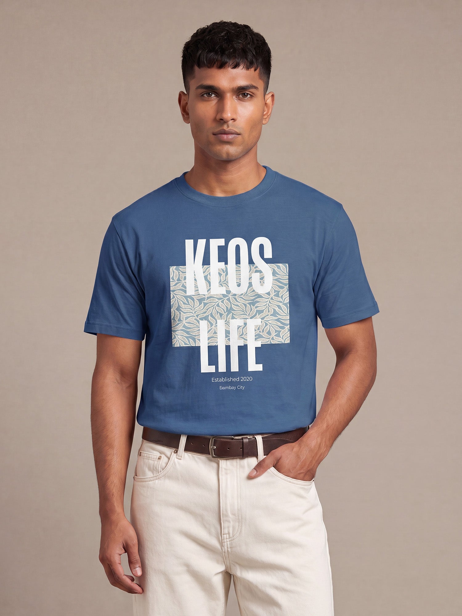 Indian male model wearing Keos Floral Block blue graphic t-shirt with white KEOS LIFE print and floral artwork, styled with off-white trousers.