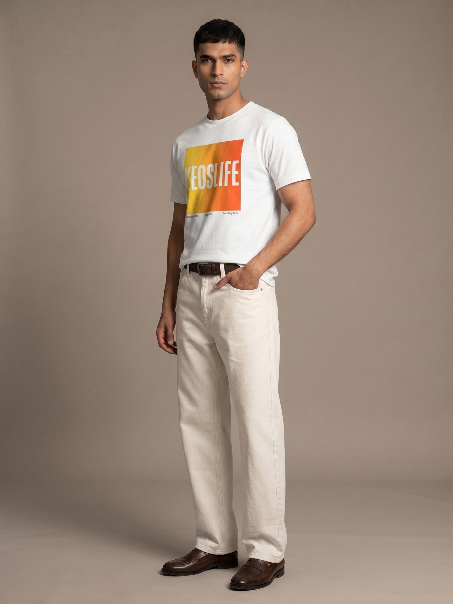 Men’s white Keos Pride Block graphic tee with yellow and orange chest print, styled with cream straight-fit jeans and brown leather shoes.