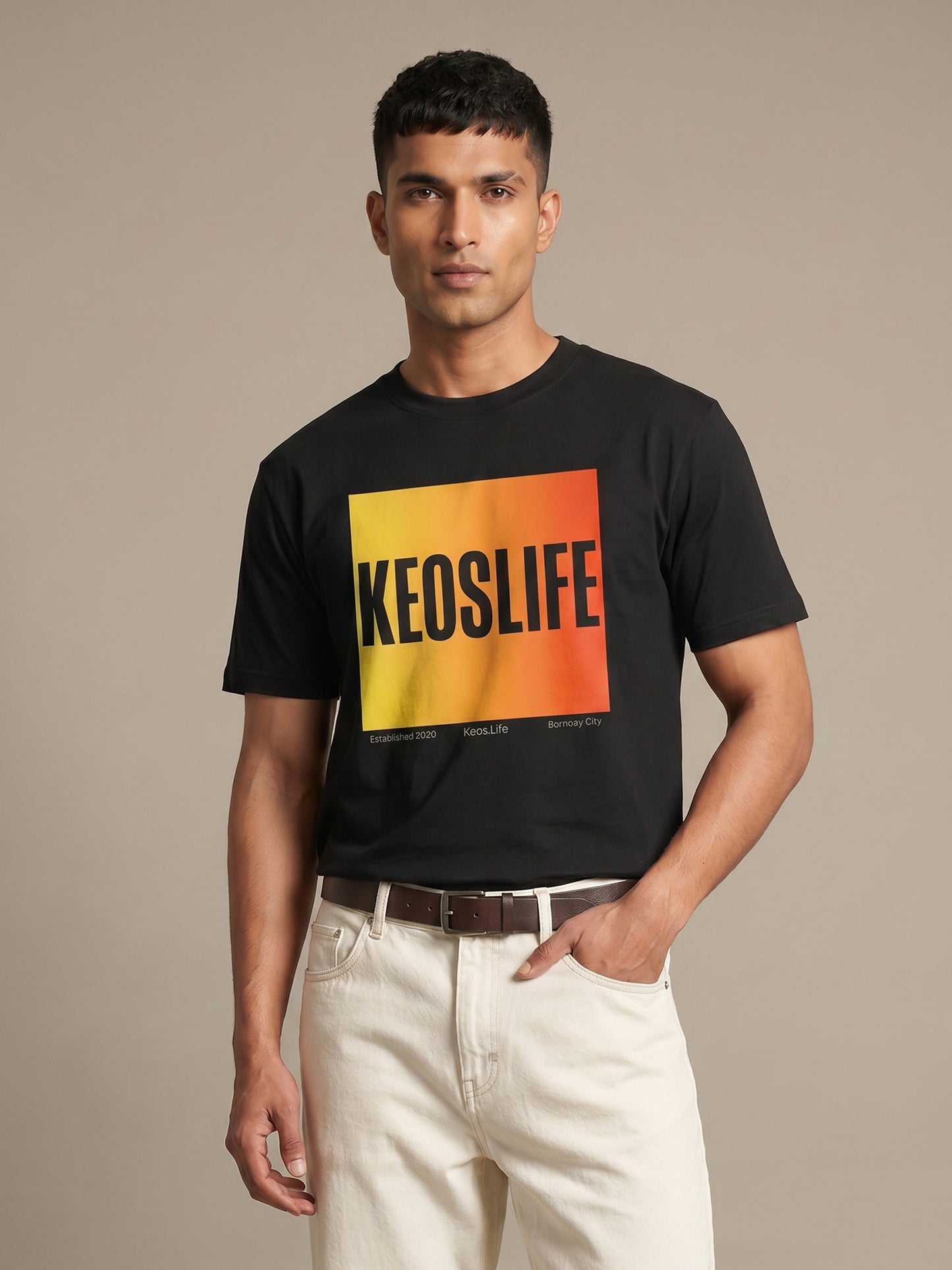 Indian male model wearing Keos Pride Block black graphic t-shirt with yellow orange KEOSLIFE print, styled with off-white trousers.
