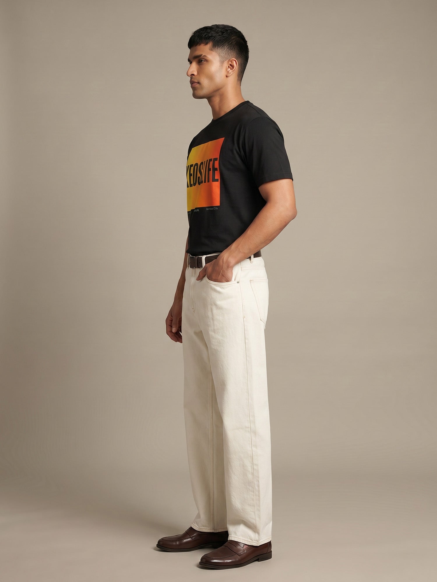 Side profile of men’s black Keos Pride Block graphic tee with yellow orange chest print, styled with off-white straight-fit jeans.