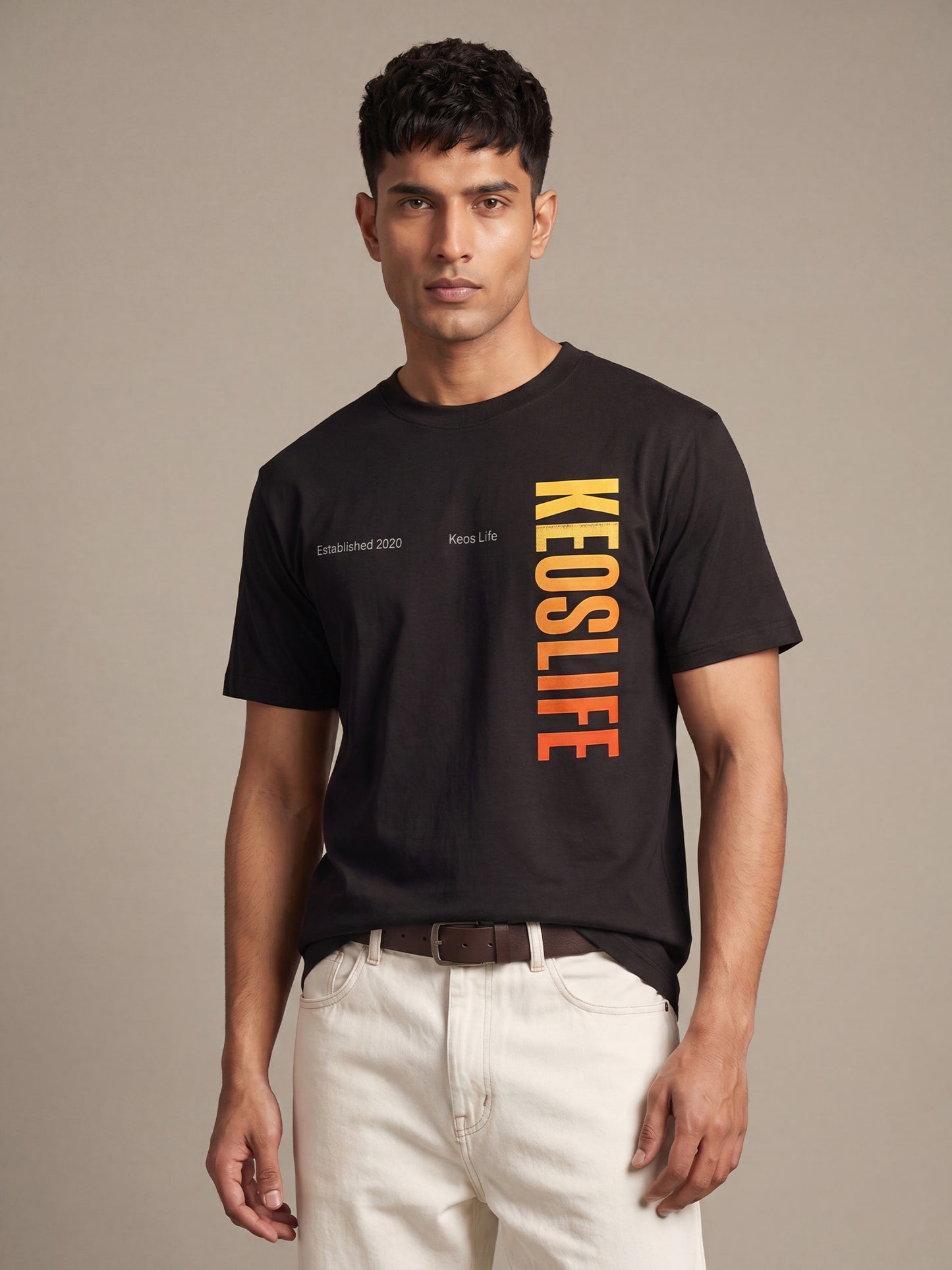 Indian male model wearing Keos Pride Bold black graphic t-shirt with vertical yellow orange KEOSLIFE print, styled with off-white trousers.