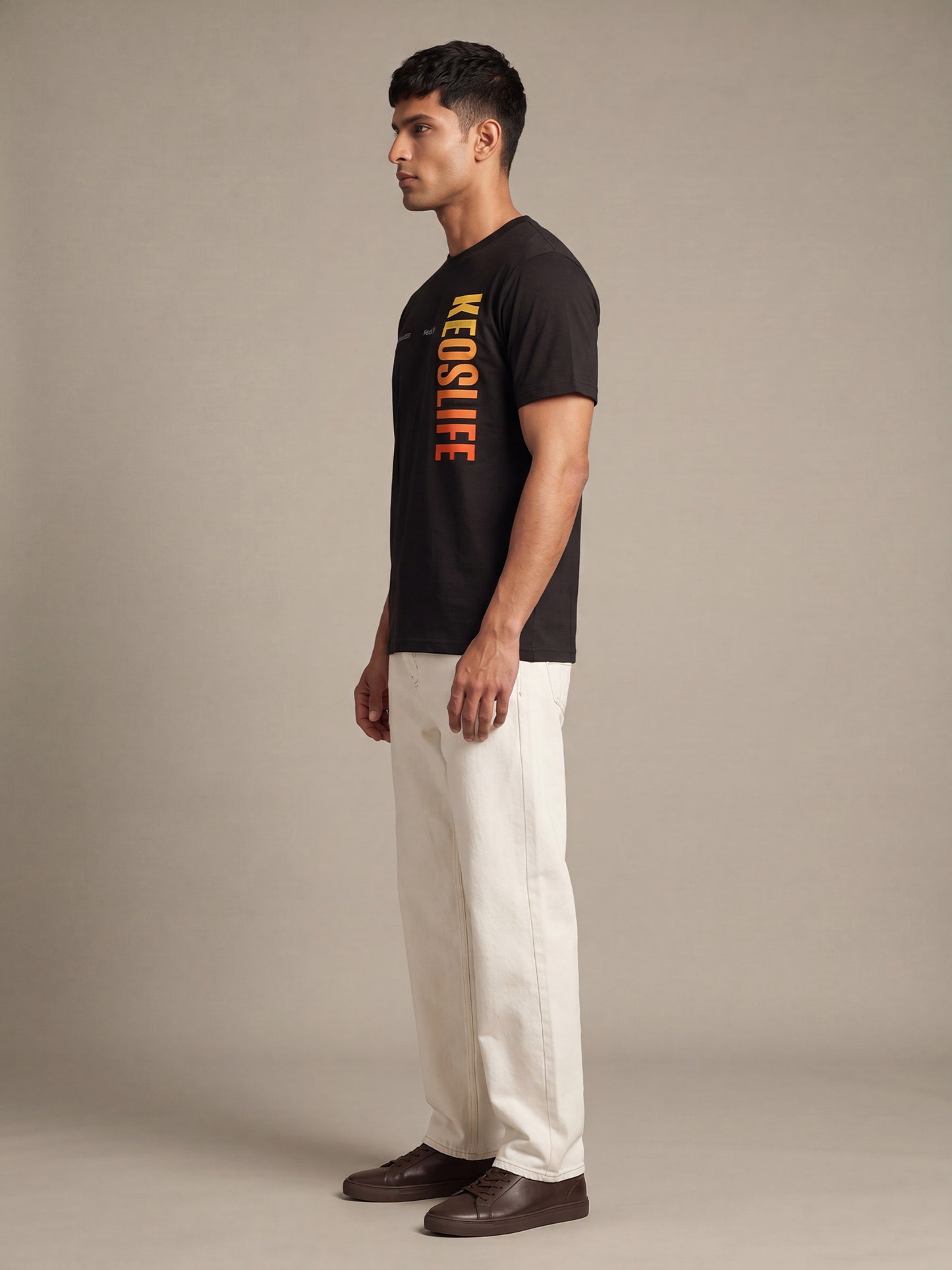 Side profile of men’s black Keos Pride Bold graphic tee with vertical yellow orange chest print and off-white straight-fit jeans.