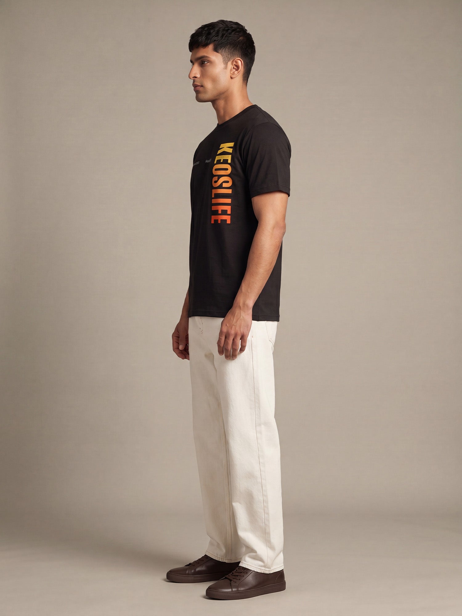 Side profile of men’s black Keos Pride Bold graphic tee with vertical yellow orange chest print and off-white straight-fit jeans.