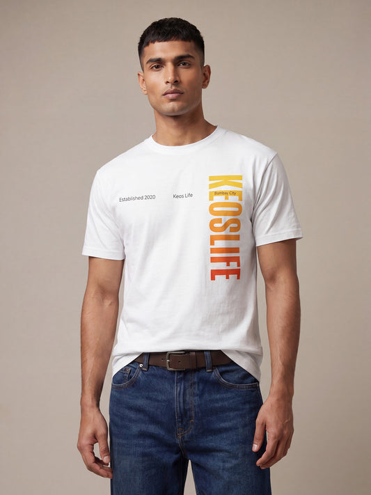Indian male model wearing Keos Pride Bold white graphic t-shirt with vertical yellow orange KEOSLIFE print, styled with blue denim jeans.