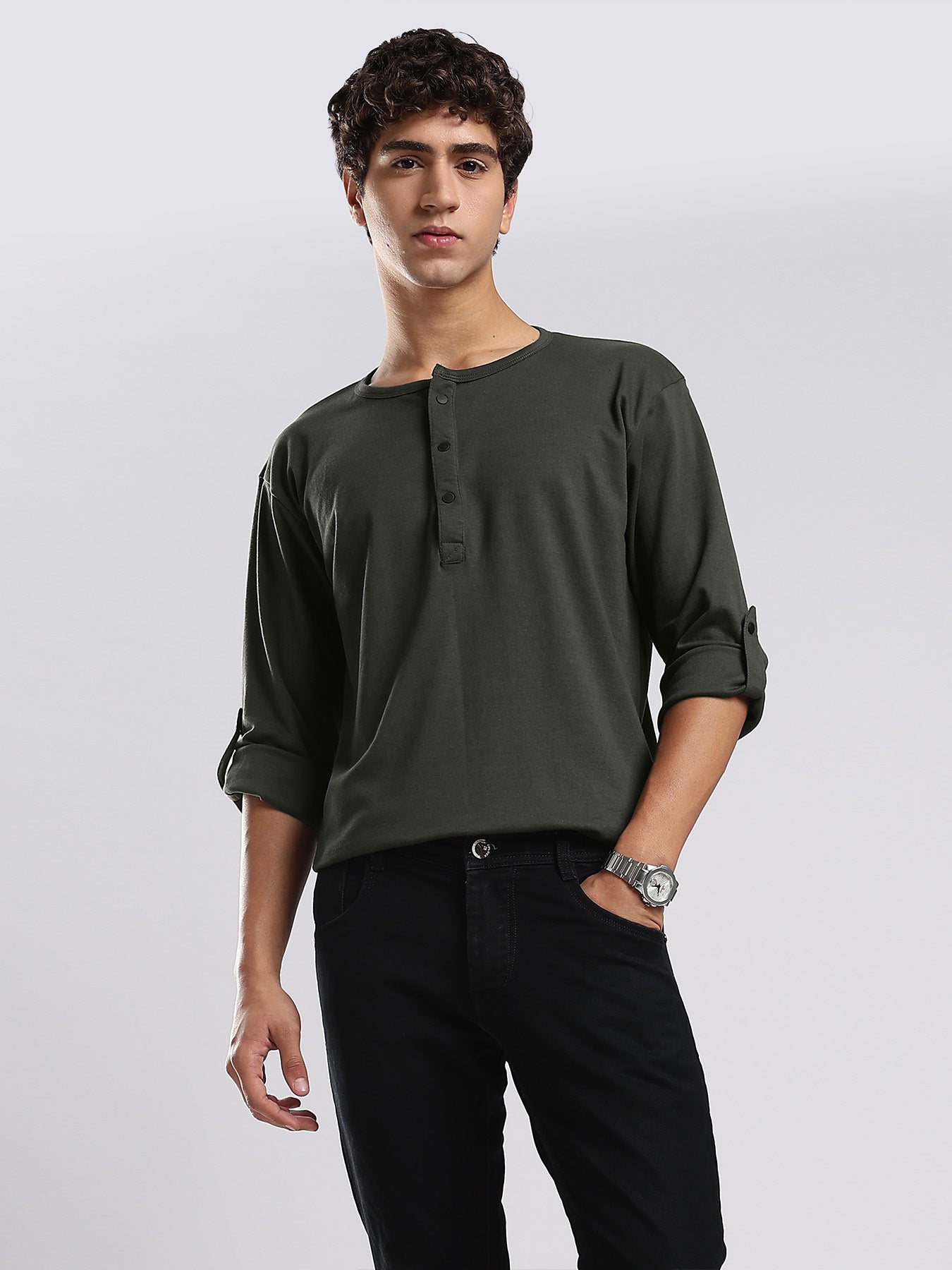 Man wearing a dark green henley shirt and black pants on a light gray background