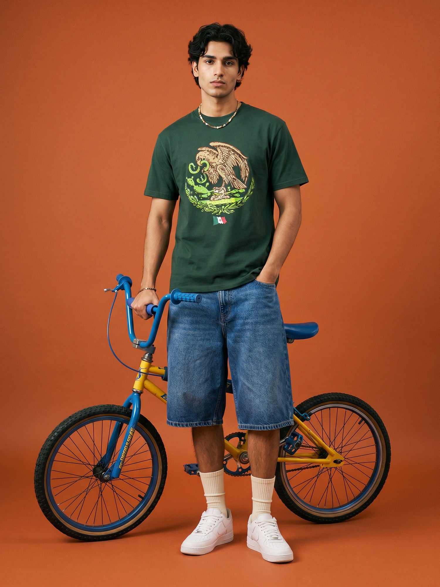 Man wearing a green t-shirt with a graphic design, standing next to a bicycle on an orange background