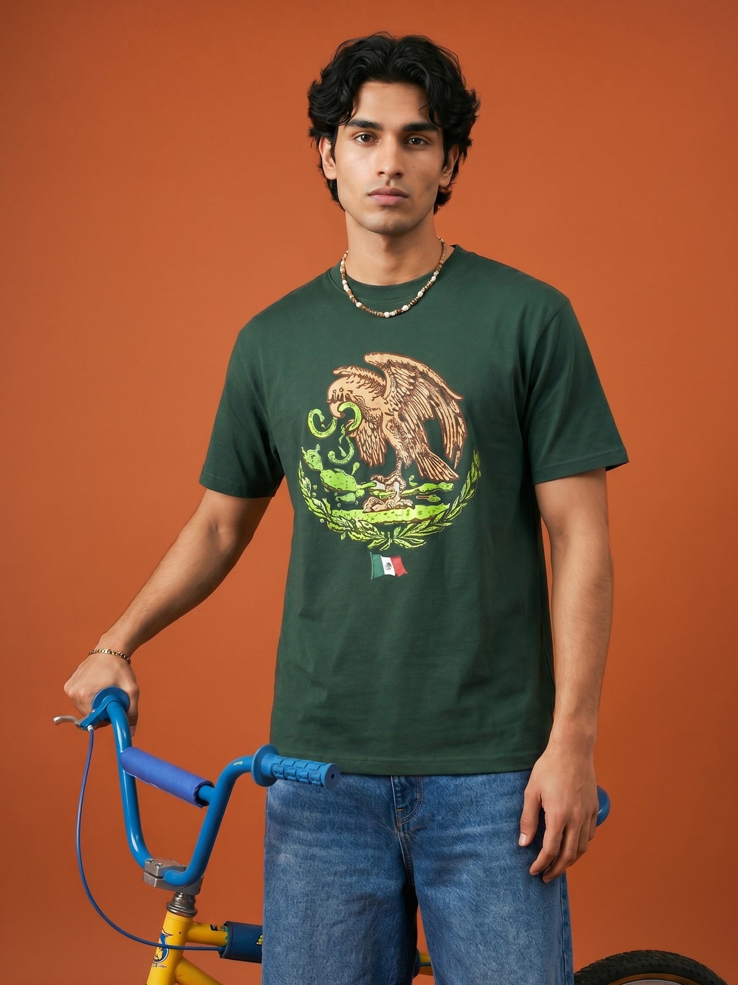 Man wearing a green t-shirt with a graphic design, standing against an orange background