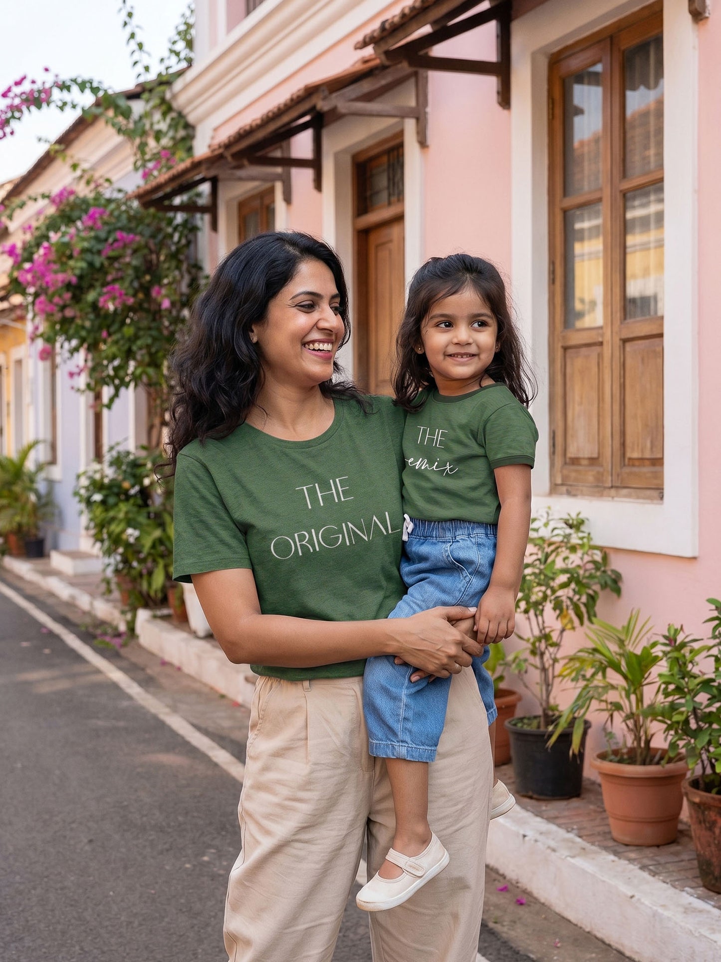 Woman and child wearing matching green t-shirts in front of a pink building.