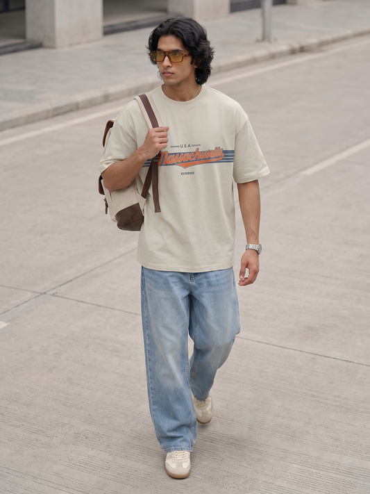 Off-White Graphic T-Shirt Keos men’s oversized graphic t-shirt with retro typography print paired with relaxed-fit denim jeans and sneakers. Modern streetwear outfit inspired by vintage Americana fashion, oversized clothing, casual everyday wear and contemporary urban style.
