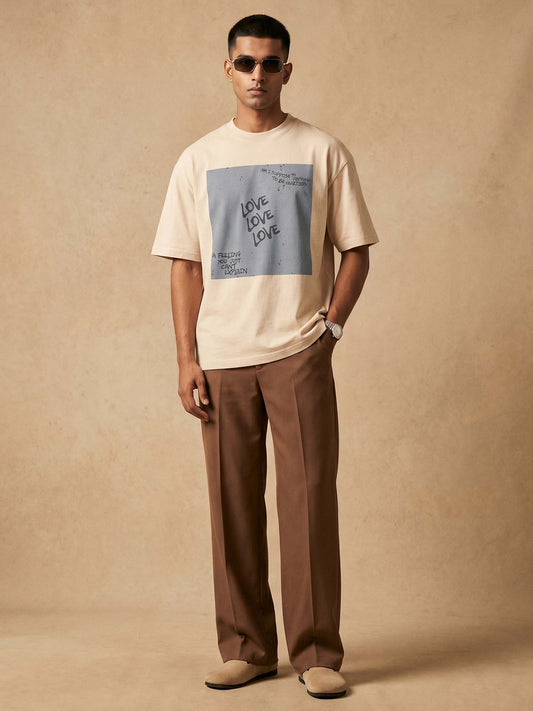 Man wearing a beige t-shirt with graphic design and brown pants against a beige background