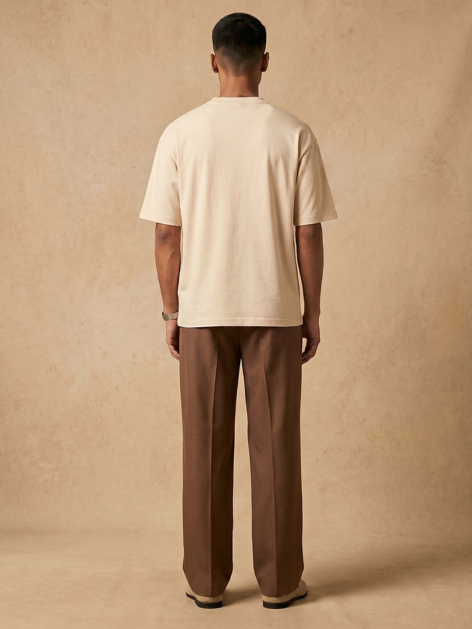 Man wearing a beige t-shirt and brown pants against a beige background