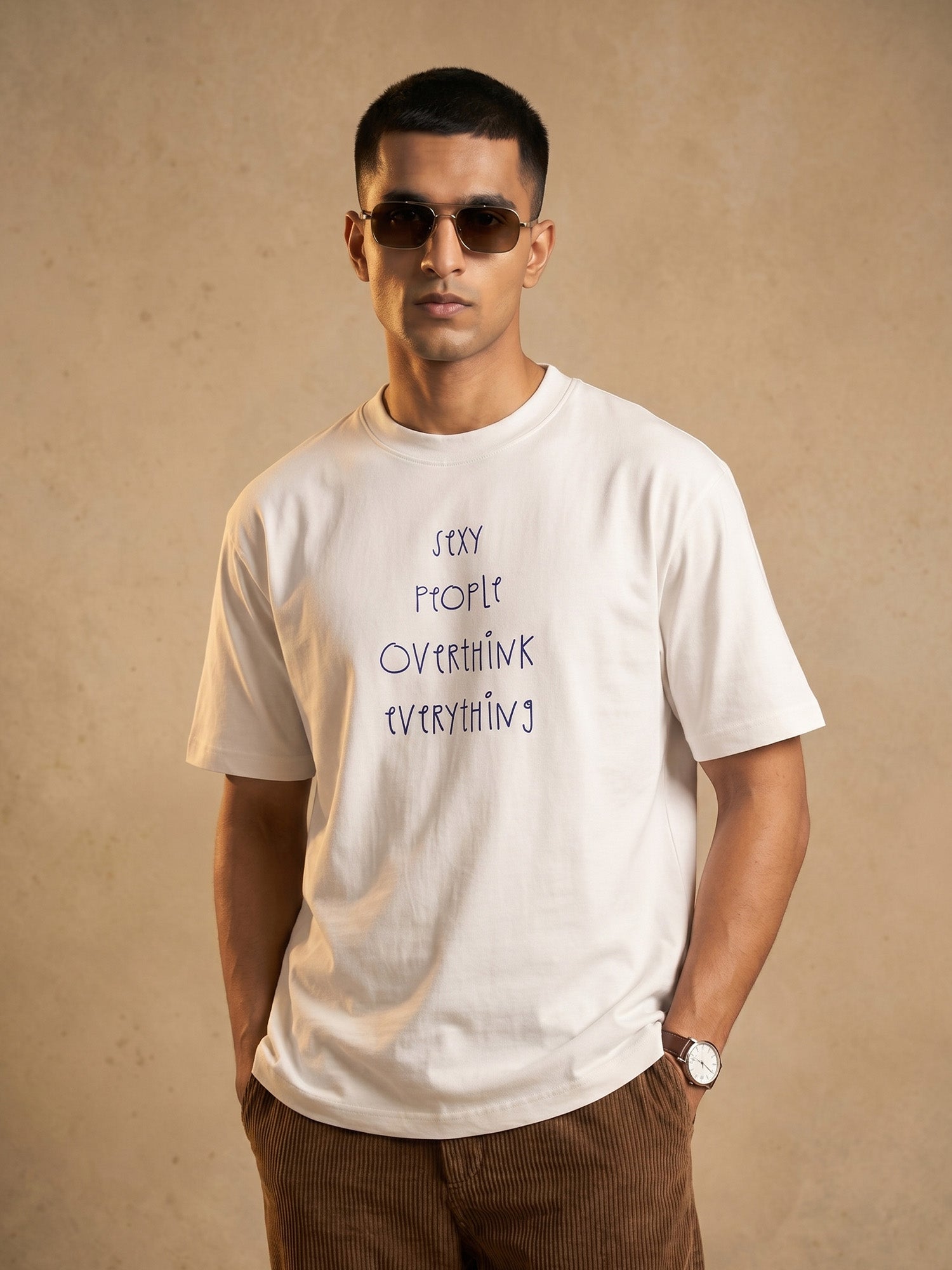 Indian male model wearing Keos Sexy People white regular-fit graphic t-shirt with handwritten text print, styled with brown corduroy trousers.