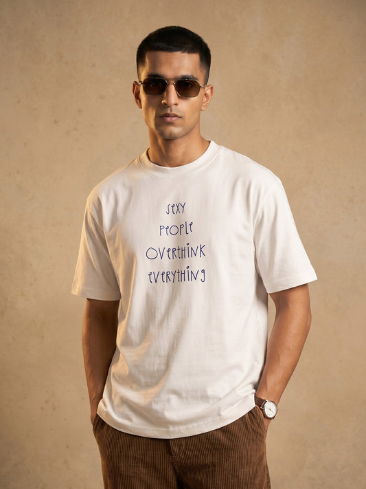 Indian male model wearing Keos Sexy People white regular-fit graphic t-shirt with handwritten text print, styled with brown corduroy trousers.