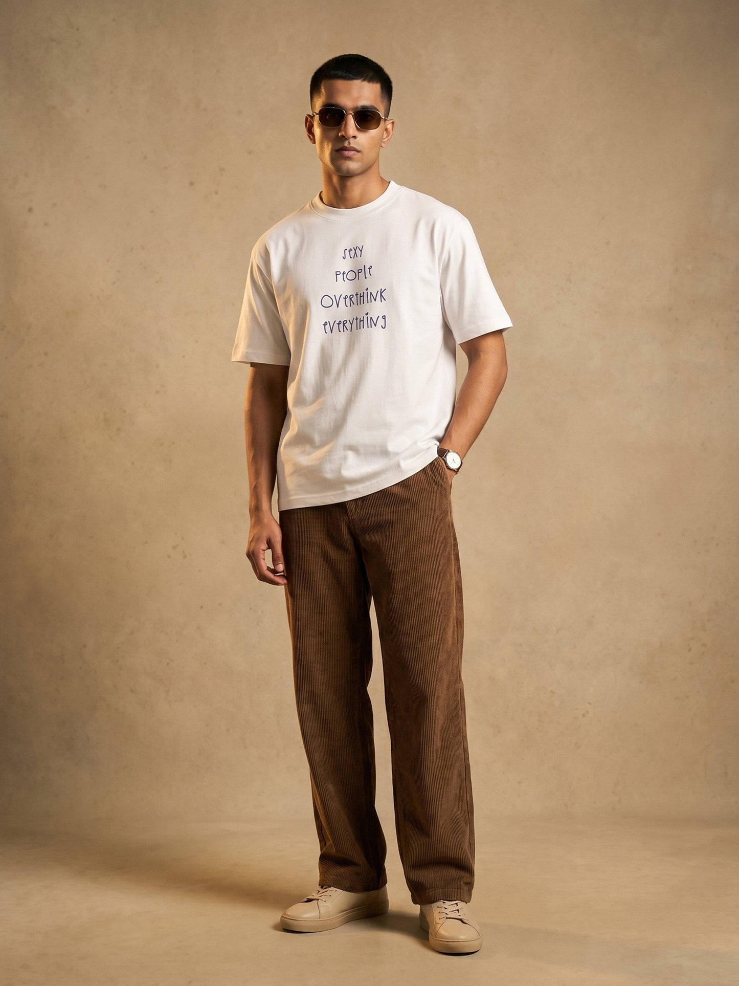 Keos white cotton graphic t-shirt for men featuring Sexy People Overthink Everything front print, styled with brown corduroy pants and sneakers.