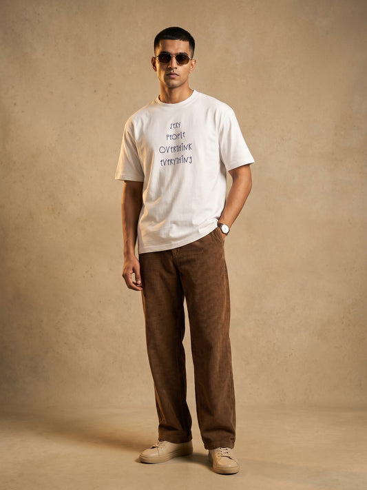 Keos white cotton graphic t-shirt for men featuring Sexy People Overthink Everything front print, styled with brown corduroy pants and sneakers.