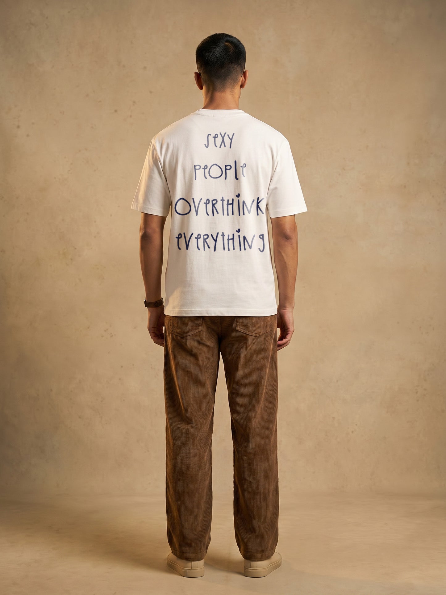 Back view of Keos Sexy People white cotton t-shirt showing large handwritten-style back print with brown corduroy trousers.
