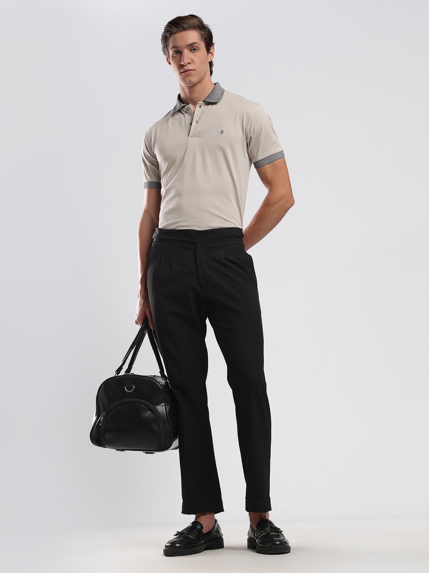 Man wearing a beige polo shirt and black pants holding a black bag on a white background