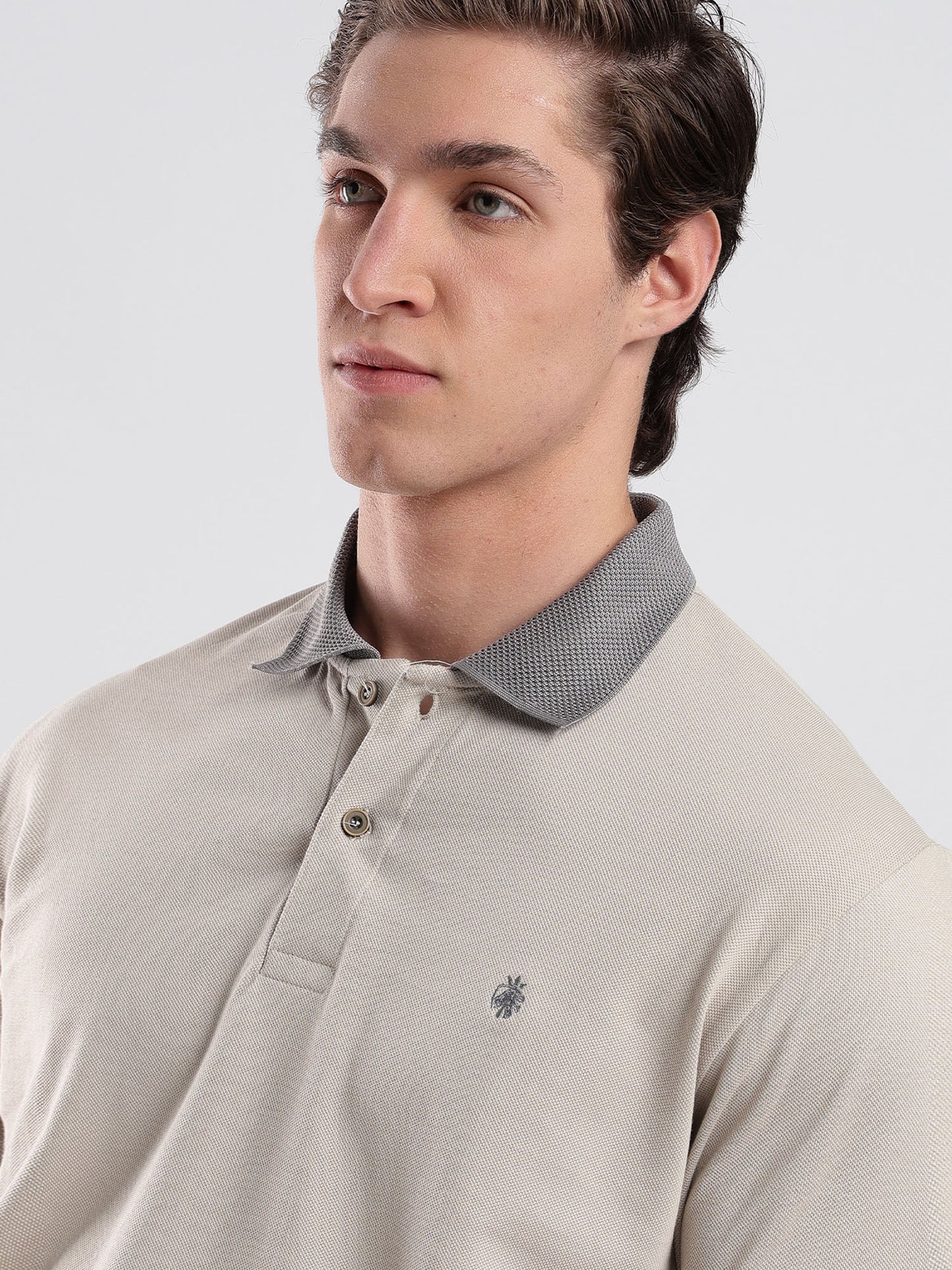 Man wearing a beige polo shirt with a small logo on a light gray background