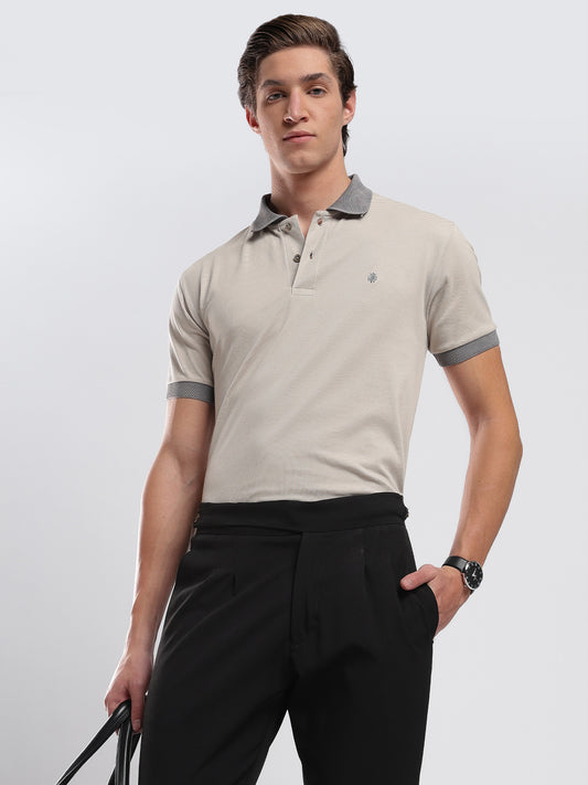Man wearing a beige polo shirt with gray accents and black pants on a light gray background