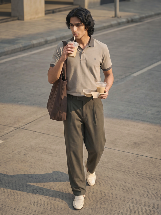 Taupe Polo Shirt Keos men’s premium taupe polo shirt styled with charcoal pleated trousers, white loafers and a brown tote bag. Model walking through a modern city street carrying iced coffee, showcasing effortless smart casual menswear, old money fashion, quiet luxury style, summer outfit inspiration and contemporary urban fashion.
